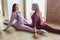Professional two female athletes are sitting in yoga position together. They are touching their arms and looking at each