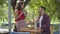 Professional waitress in red blouse and skirt pouring hot tea to her client who sitting at the table smiling and