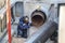 Professional welder welding water or gas steel pipeline in protective trench and mask at construction site pit. City underground