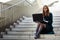 Professional woman wearing glasses and sitting in a staircase with a laptop in her legs