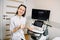 Professional young woman doctor sonographer sitting nearby modern ultrasound scanner machine and smiling