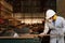 Professional young worker in white uniform and safety equipment cutting a piece of wood on table saw machine in carpentry factory.