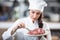 Professionally dressed chef brushes raw steak on a plate with spring of fresh rosemary