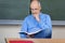 Professor Reading Book At Desk In Classroom