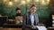 Professor and secretary or assistant working at his desk with vintage typewriter front of a blackboard.