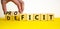 Proficit or deficit symbol. Businessman turns cubes, changes the word deficit to proficit. Beautiful yellow table, white