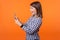 Profile of amazed beautiful brunette woman with charming smile in checkered shirt holding cellphone. indoor studio shot isolated