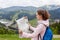 Profile of attractive young tourist being lost on her way, looking at map attentively, searching for proper route, standing at