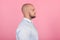 profile of a beautiful bald man with a beard dressed in a white shirt. stands in front of the pink background