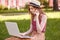 Profile of busy pensive curly haired girl working in park with laptop, sitting on grass, searching for information, talking over
