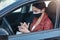 Profile of busy serious young female driving car, wearing medical mask for protection, holding mobile phone, using device, reading