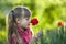 Profile of cute pretty smiling child girl with gray eyes and long hair smelling bright red tulip flower on blurred sunny summer