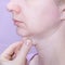 A profile of a european woman pinching her double chin with fingers against pink background