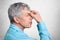 Profile of exhausted grey haired male in formal shirt, keepd hands on nose, poses against white concrete background, tries to conc