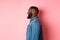 Profile of handsome bearded Black guy standing over pink background, smiling and looking left at copy space