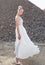 Profile image of the blonde young woman in a white wedding dress, posed behind piles of stones during the day