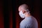 Profile of a man in medical gauze mask standing on dark red background. Protection of upper and lower respiratory tract