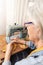 profile of older woman in front of an antique sewing machine cutting a thread from an orange fabric