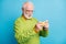 Profile photo of angry grandpa hold smartphone tense play game wear specs green sweater isolated blue color background