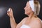 Profile photo. Senior woman with a bandage on her head sprays facial spray on a black background.