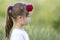 Profile portrait of cute small serious girl in white T-shirt with long blond pony-tail and red rose in hair on blurred bright gree