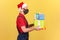Profile portrait deliveryman in uniform, red santa claus hat and surgical medical mask holding parcels and gifts, delivery on