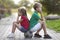 Profile portrait of two cute blond children, smiling boy and long-haired girl sitting on soccer ball on empty sunny suburb paved