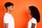 Profile portrait of two dark skin young persons look each other isolated on orange color background