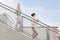 Profile shot of businesswomen holding disposable cup and mobile phone while moving down stairs together against sky