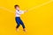 Profile side full length photo of small boy playing tug war game losing heavy challenge  vibrant color
