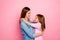 Profile side photo of lovely lady cuddling her kid looking wearing denim jeans shirt isolated over pink background