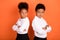 Profile side photo of two young black kids folded hands unhappy offended conflict isolated over orange color background