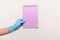 Profile side view closeup of human hand in blue surgical gloves holding purple notepad in hand and holding empty paper