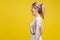 Profile side view of happy amazed blonde woman with ponytale hairstyle and in casual beige blouse, isolated on yellow background