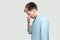 Profile side view portrait of depressed sad handsome young man in light blue shirt standing, covering his eyes and crying