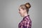 Profile side view of scared blonde girl in red, pink checkered shirt, collected bun hairstyle standing and looking aside and