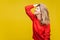 Profile side view of sensual happy blonde woman with red lipstick in casual sweater, isolated on yellow background