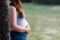 Profile of an unrecognizable pregnant woman leaning on a tree in a park