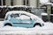 Profile view of blue Peugeot 107 car covered by the snow parked in the street by snowy day