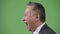 Profile view of mature angry Japanese businessman shouting against green background