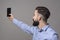 Profile view of young modern handsome bearded business man taking selfie photo with smartphone