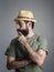 Profile view of young pensive bearded man wearing straw hat touching his beard