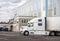 Profile of white modern big rig semi truck with refrigerated semi trailer standing on warehouse parking lot