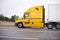 Profile of yellow big rig semi truck with semi trailer running o