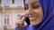 Profile of young beautiful muslim woman in hijab talking on cell phone, building in background