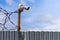 Profiled sheet fence with cheap surveillance camera and barbwire with selective focus.