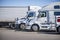 Profiles of different white big rigs semi trucks with semi trailers standing on the truck stop parking lot taking a break