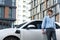 Progressive businessman with EV car at public parking car charging station.