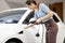 Progressive woman recharge her EV car at home charging station.