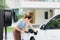 Progressive woman recharge her EV car at home charging station.